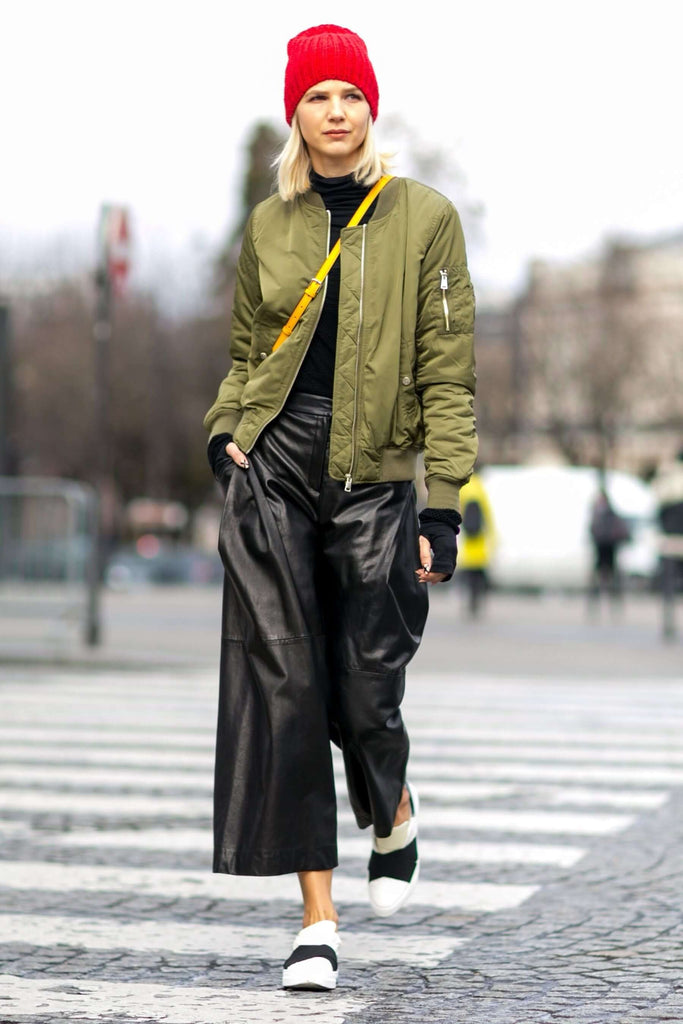 Fashionable woman in green bomber jacket and black leather trousers, walking on street with confidence.